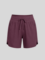 A pair of women's athletic shorts in a deep plum purple color, featuring an elastic waistband with a matching drawstring, side pockets, and a curved hem 