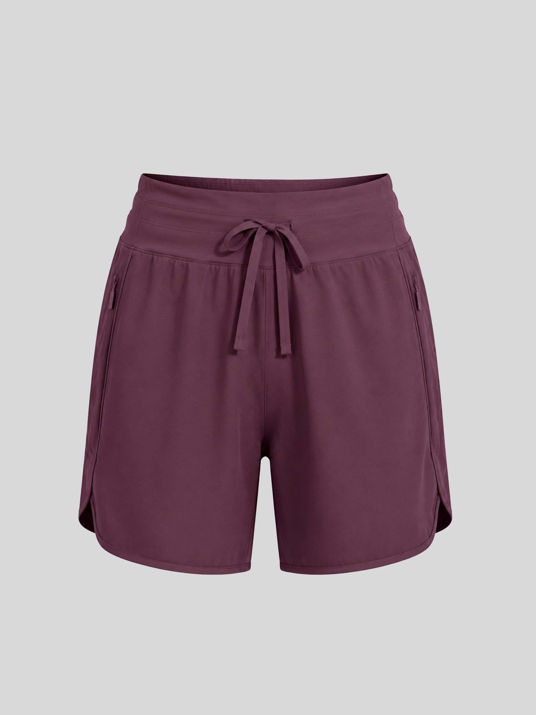 A pair of women's athletic shorts in a deep plum purple color, featuring an elastic waistband with a matching drawstring, side pockets, and a curved hem 