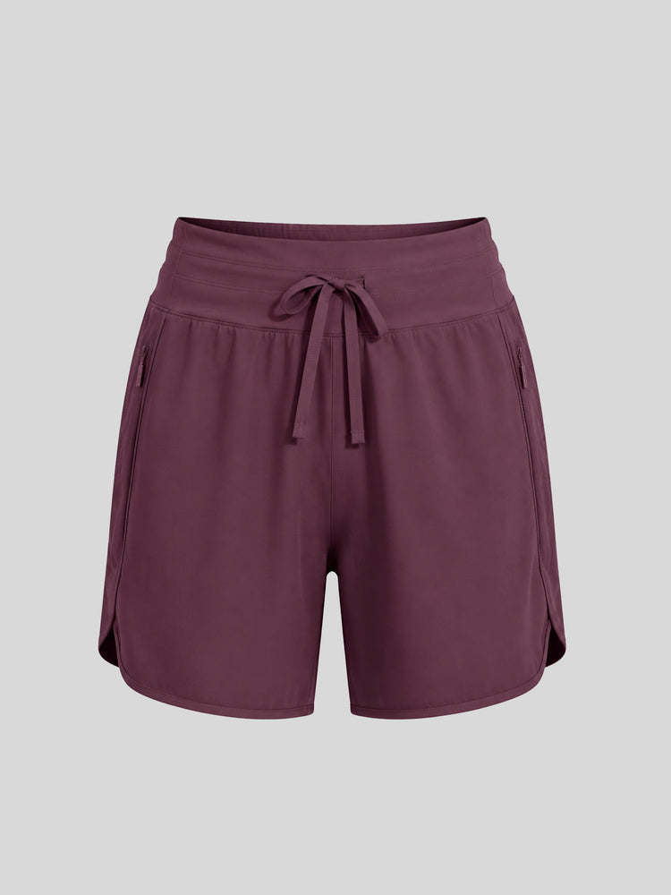 A pair of women's athletic shorts in a deep plum purple color, featuring an elastic waistband with a matching drawstring, side pockets, and a curved hem 