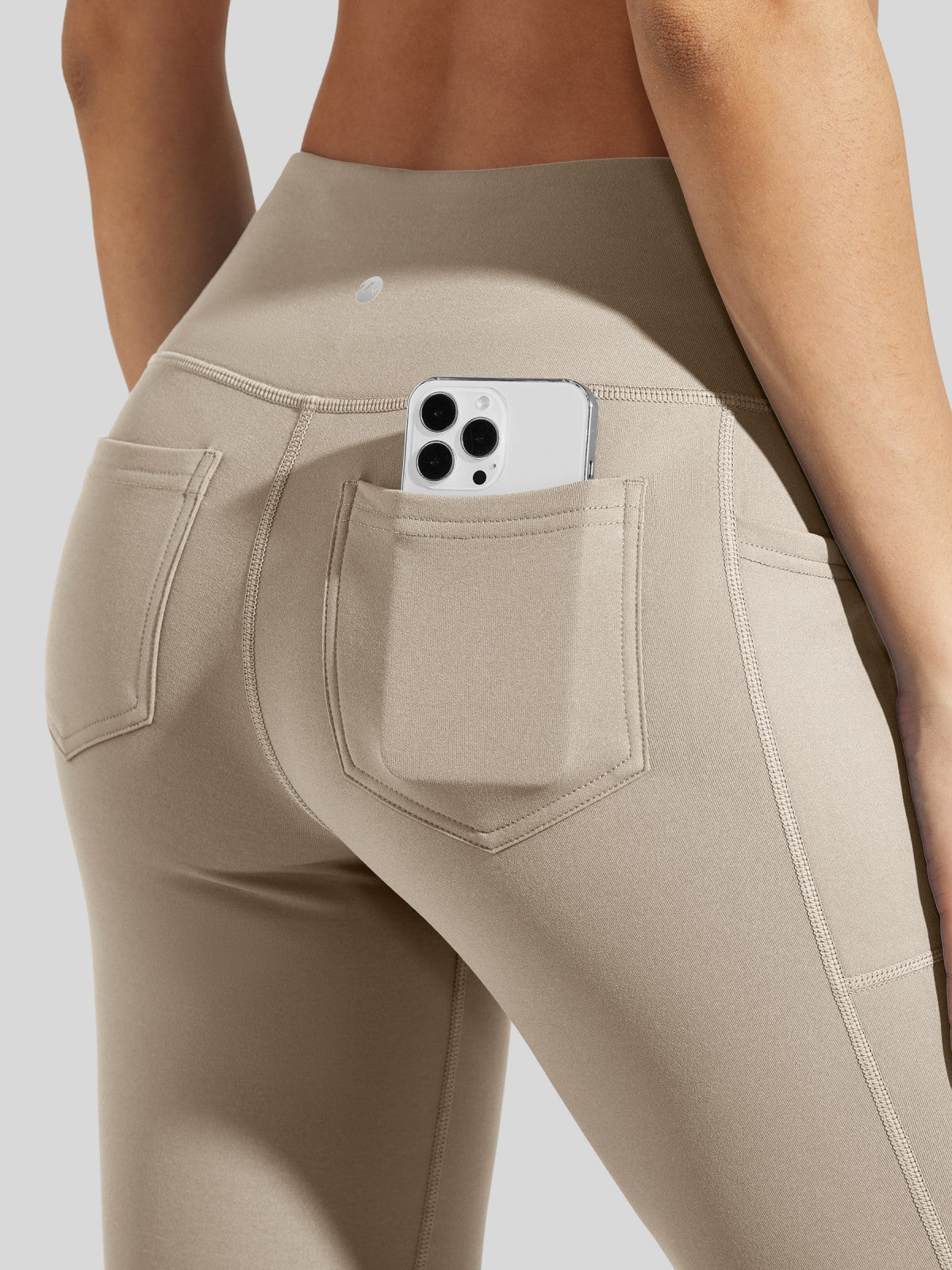 Close-up of a model wearing high-waisted beige leggings with a side pocket holding a phone 