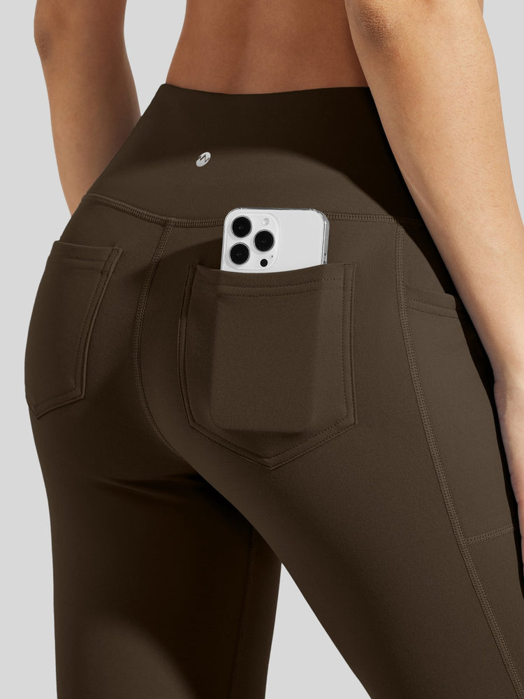 Close-up back view of a person wearing dark brown high-waisted leggings with a side pocket holding a phone 