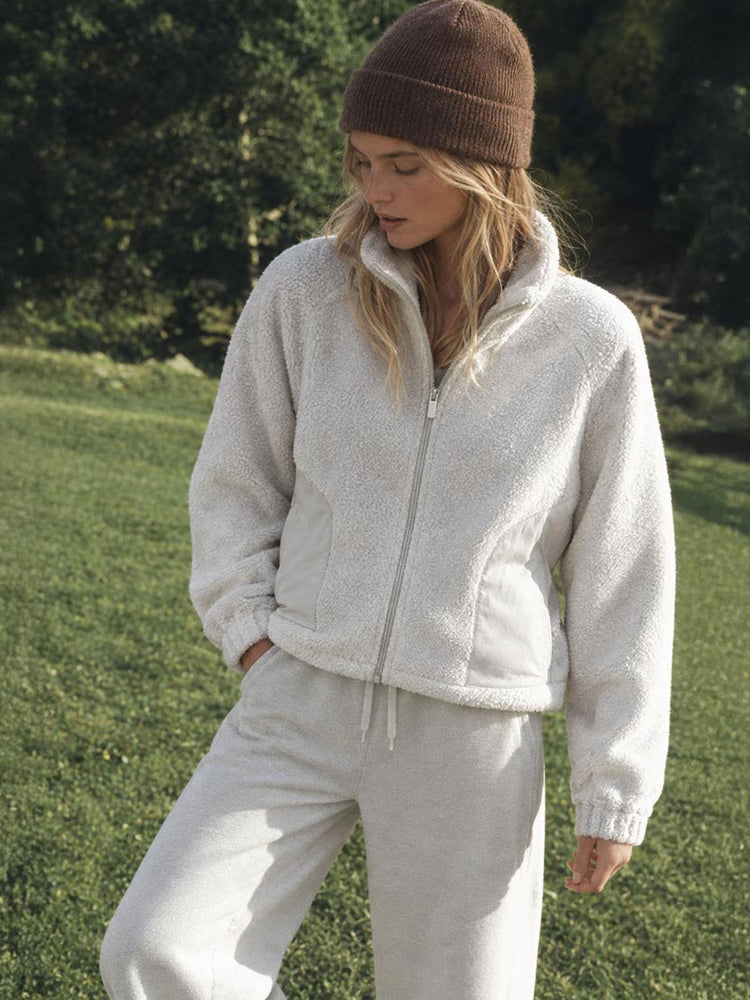 A woman wearing a cozy cream-colored fleece zip-up jacket and matching sweatpants 