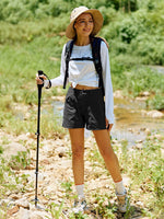 A woman hiking outdoors on a rocky path near a stream, wearing black hiking shorts 