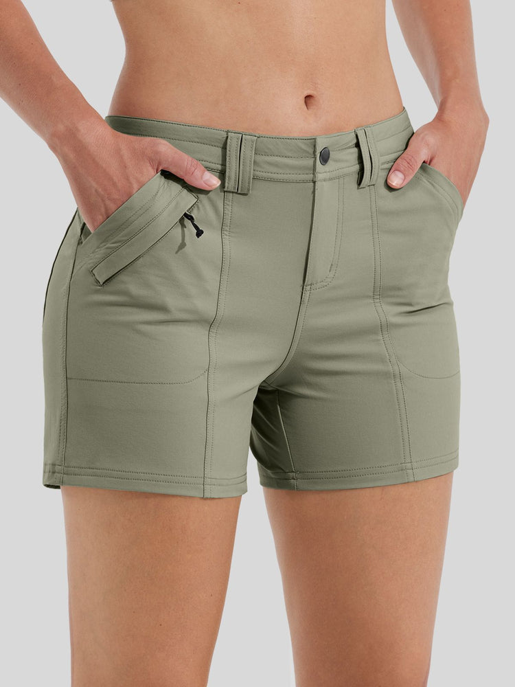 A close-up of a woman wearing olive green outdoor shorts with side pockets and a button closure  