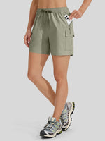 A model wearing sage green athletic shorts with a drawstring waist and a side cargo pocket holding a phone, 