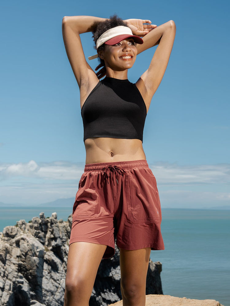 A woman posing outdoors on a rocky cliffside, wearing rust-colored drawstring shorts 