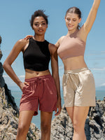 Two women standing outdoors on rocky cliffs by the sea, wearing lightweight athletic shorts 