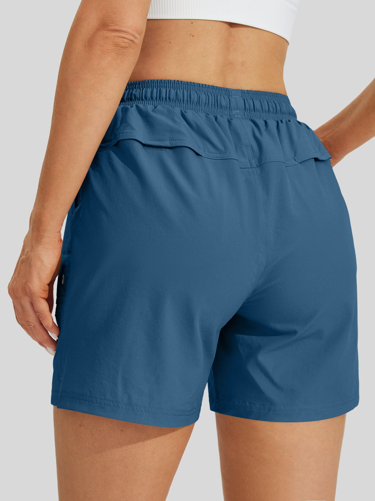 A close-up back view of a model wearing slate blue athletic shorts with an elastic waistband and side pockets 
