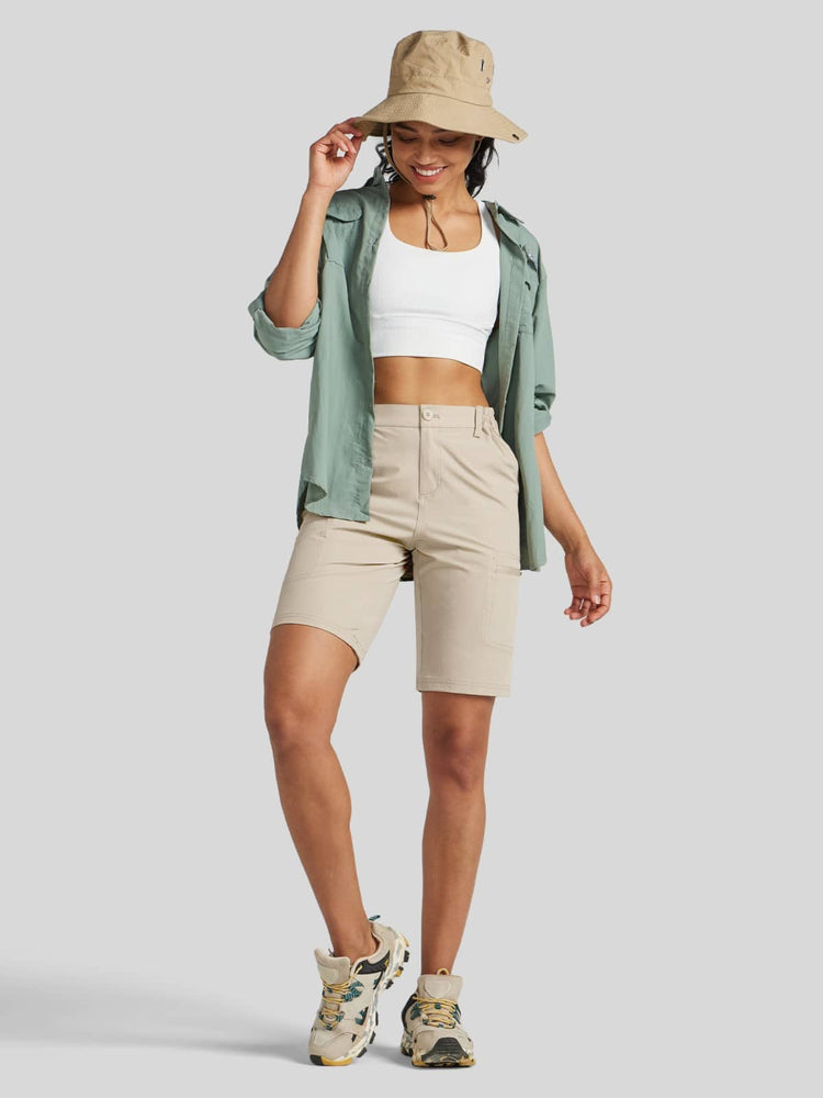 A woman modeling a light sage green lightweight overshirt, beige shorts, a white crop top, a beige bucket hat, Women's Outdoor Cargo Shorts 10 Inch Inseam 