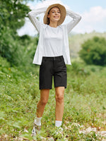 A woman standing outdoors in a grassy field wearing black hiking shorts 