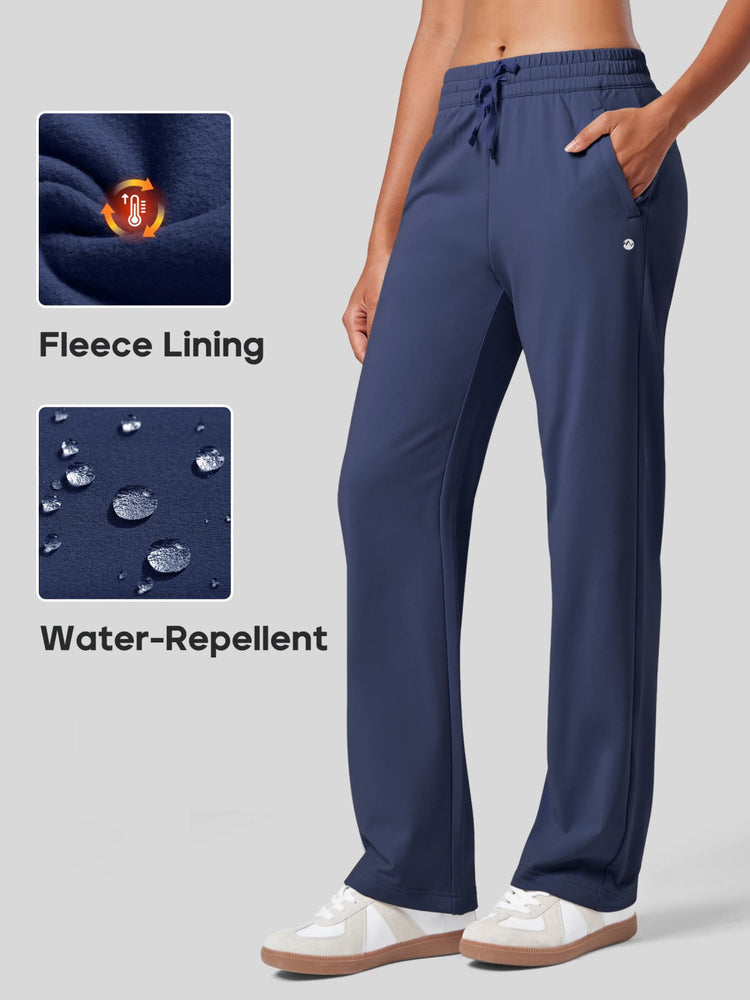 Woman wearing navy blue drawstring sweatpants with pockets, shown from the waist down on a light gray background. Fabric features fleece lining and water-repellent 
