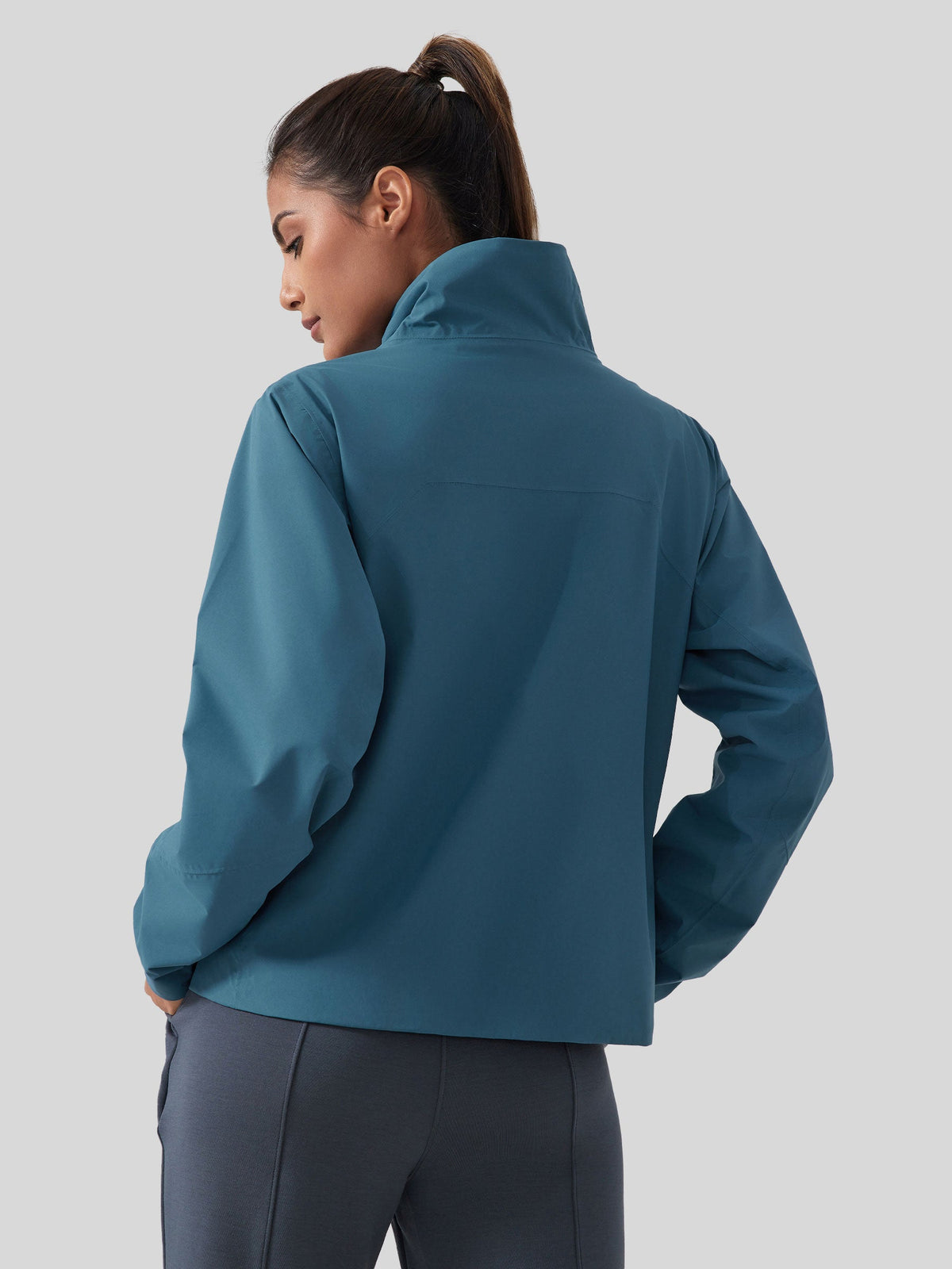 A woman shown from the back wearing a teal blue high-collar jacket fleece linend 