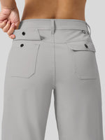 Close-up back view of a woman wearing light gray high-waisted pants, showing the waistband, belt loops, and two flap back pockets with dark buttons. 