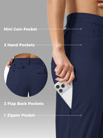 Close-up of a person wearing navy blue pants with labeled feature callouts: Mini Coin Pocket, 2 Hand Pockets, 2 Flap Back Pockets, and 1 Zipper Pocket. A phone is tucked into the side pocket to demonstrate storage. 
